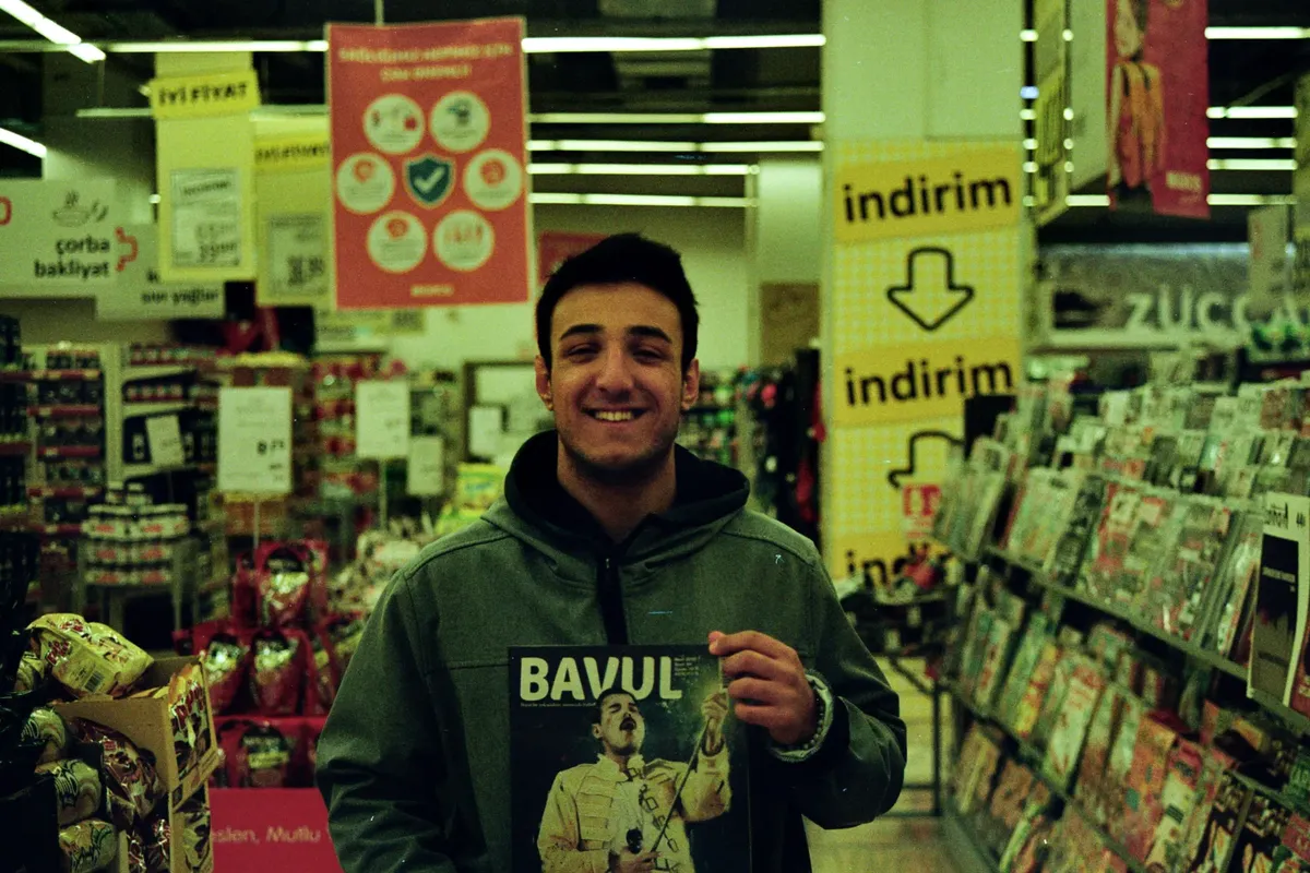A man smiling while holding a magazine in a vibrant Turkish store setting.