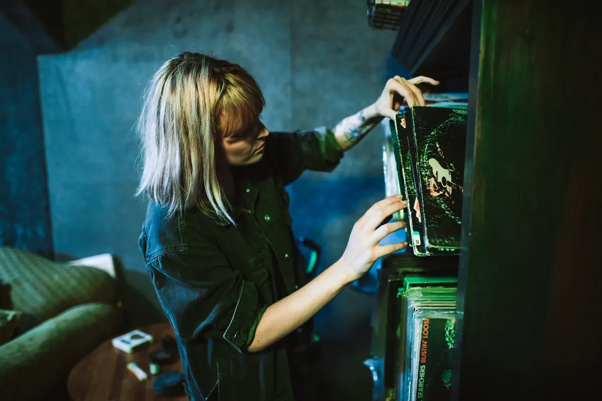 A woman in a music studio choosing vinyl records from a shelf.
