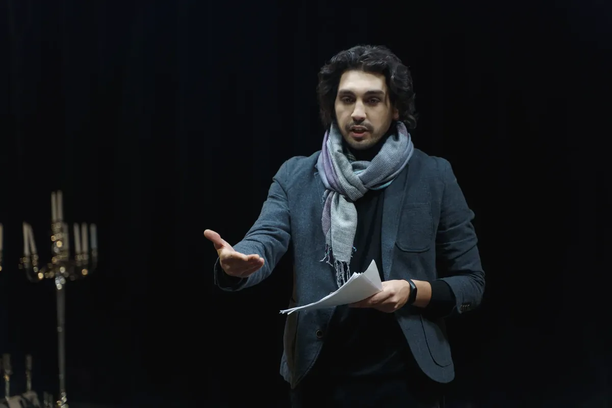 Actor rehearsing on a dark theater stage, holding a script and gesturing dynamically.